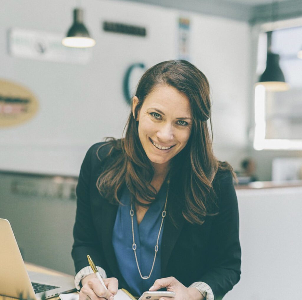 Hammersmith Support | An Interview with Lyndsay Clements, Owner of Ellen Grace Marketing women in blazer and denim shirt looks up smiling from computer ellen grace marketing